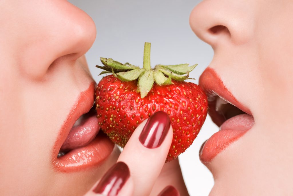 Female lovers enjoying erotic act with fresh strawberrie