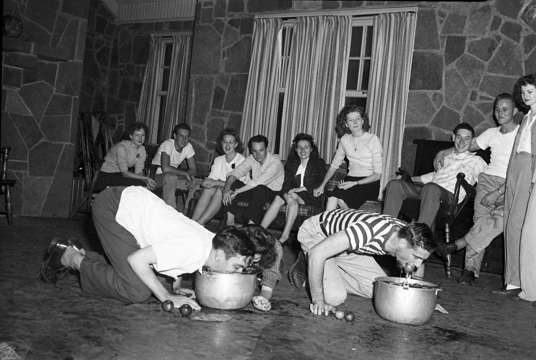 Young people bobbing for apples at a Halloween party, black and white photograph