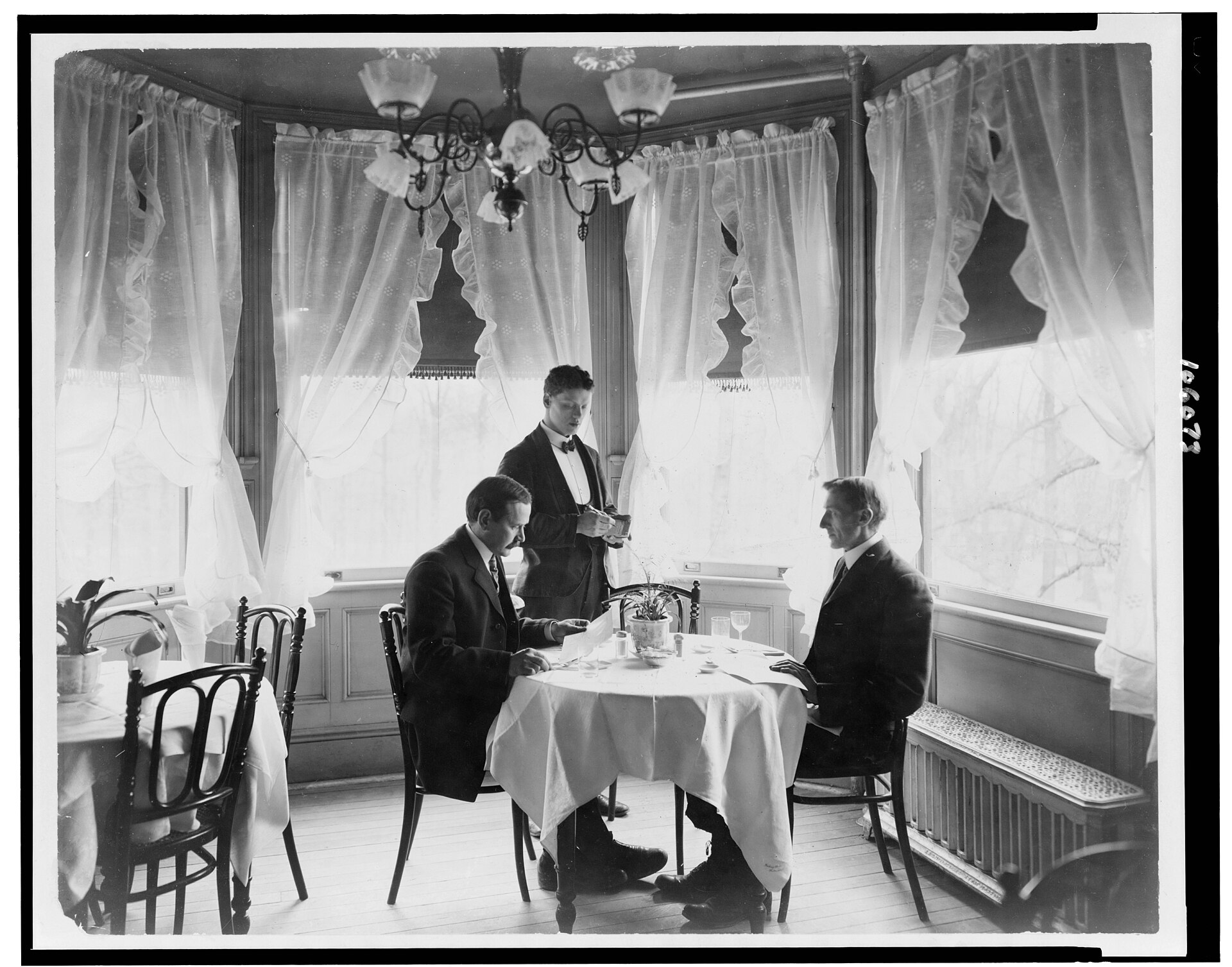 A waiter serving diners in an early twentieth-century restaurant